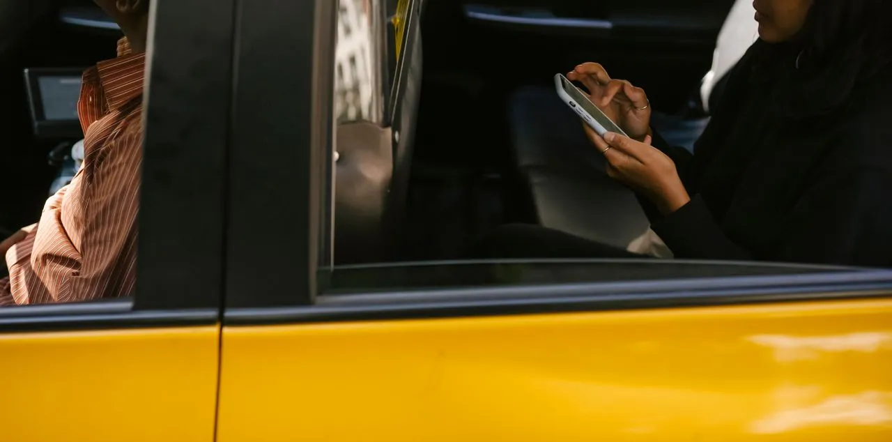 A passenger typing on her phone in the back of a yellow car